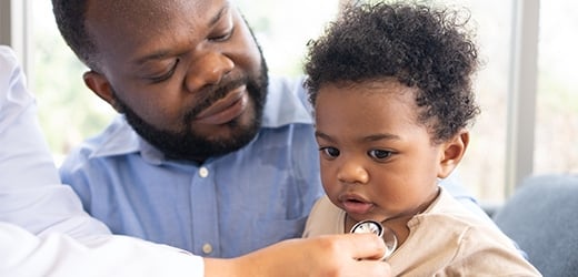 Man holding a child who is being examined by a doctor
