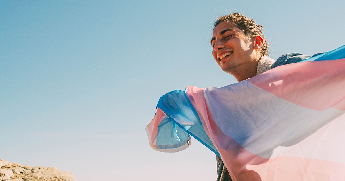 A happy young transgender man with the transgender flag.